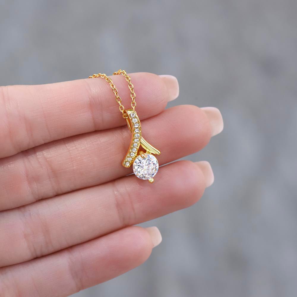 Gold necklace with a diamond pendant held between fingers against a blurred background