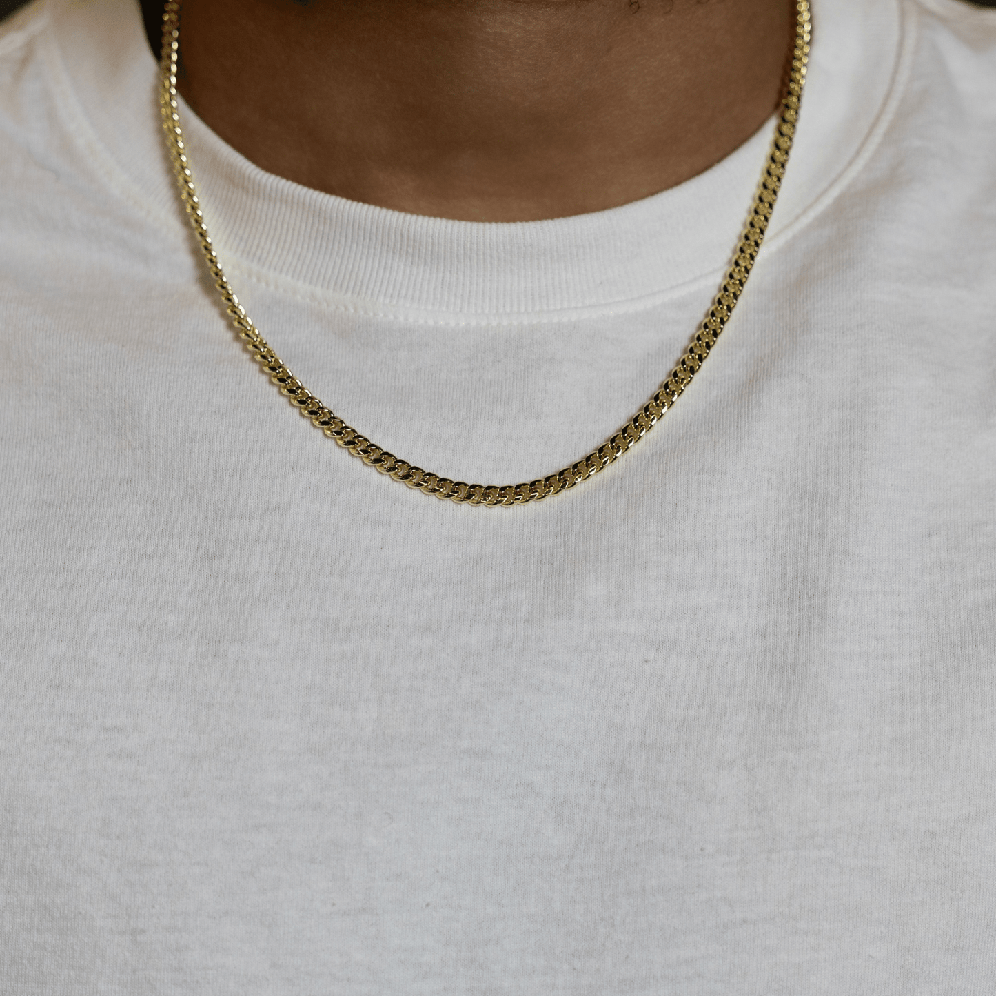 A close-up of a person wearing a gold chain necklace over a white crewneck sweatshirt.