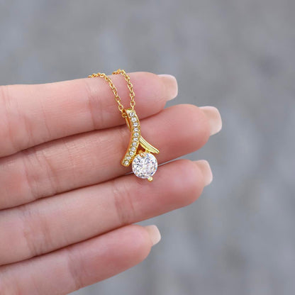 Gold necklace with a diamond pendant held between fingers against a blurred background
