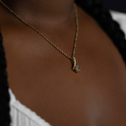 person wearing a gold chain necklace with a small silver pendant featuring a clear gemstone, shown against dark brown skin