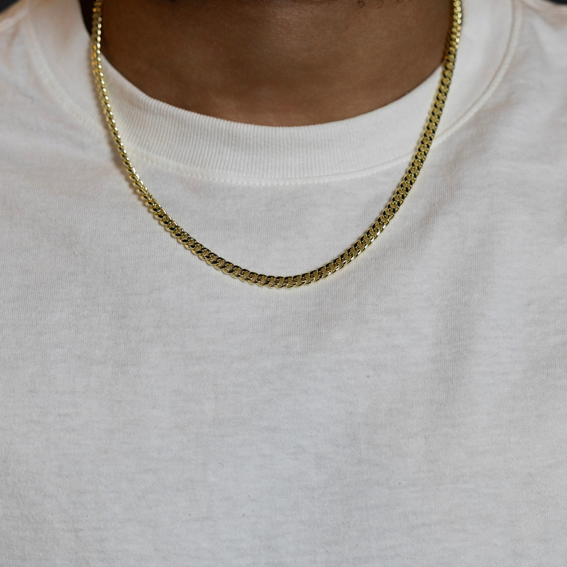A close-up of a person wearing a gold chain necklace over a white crewneck sweatshirt.