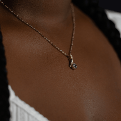 person wearing a gold chain necklace with a small silver pendant featuring a clear gemstone, shown against dark brown skin