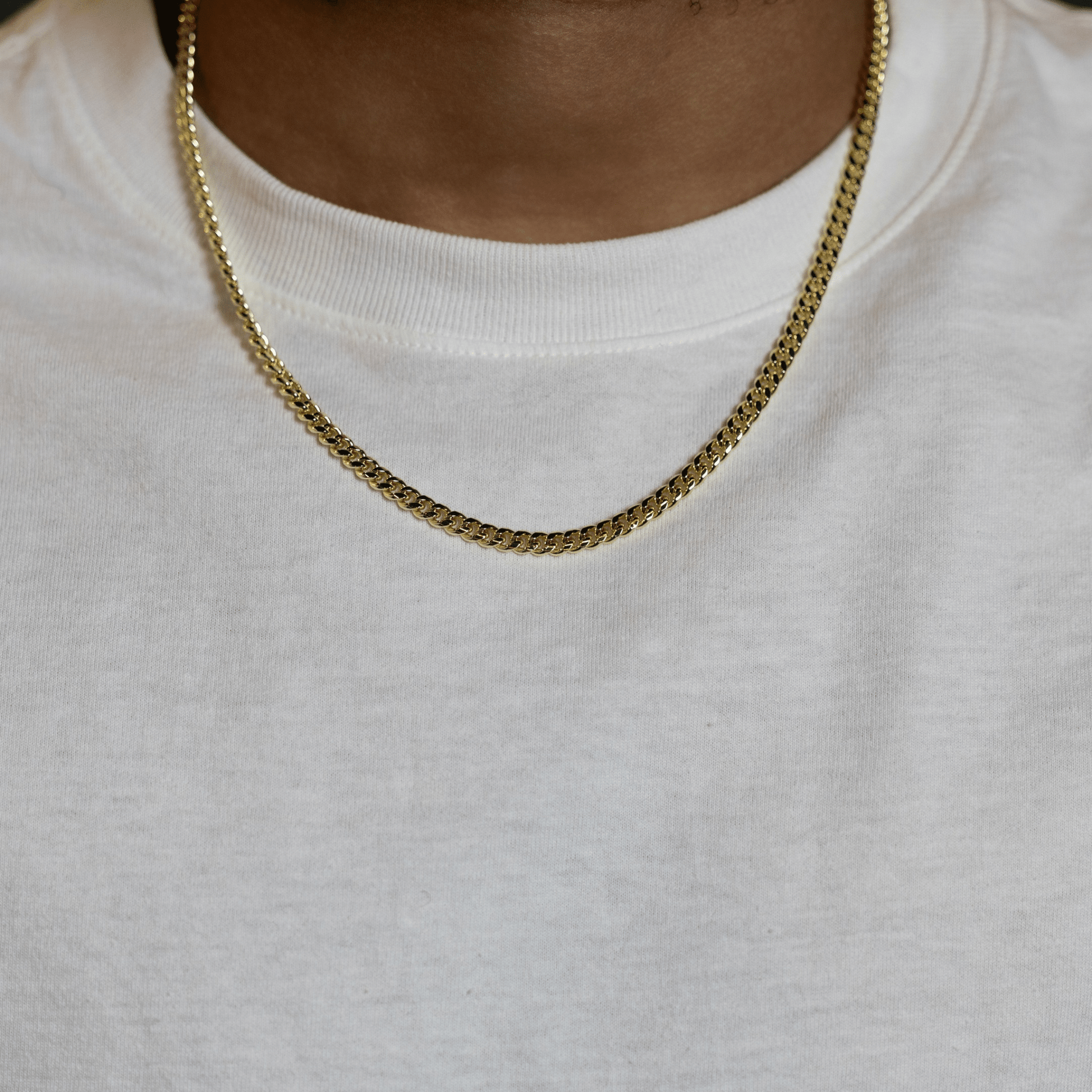 A close-up of a person wearing a gold chain necklace over a white crewneck sweatshirt.
