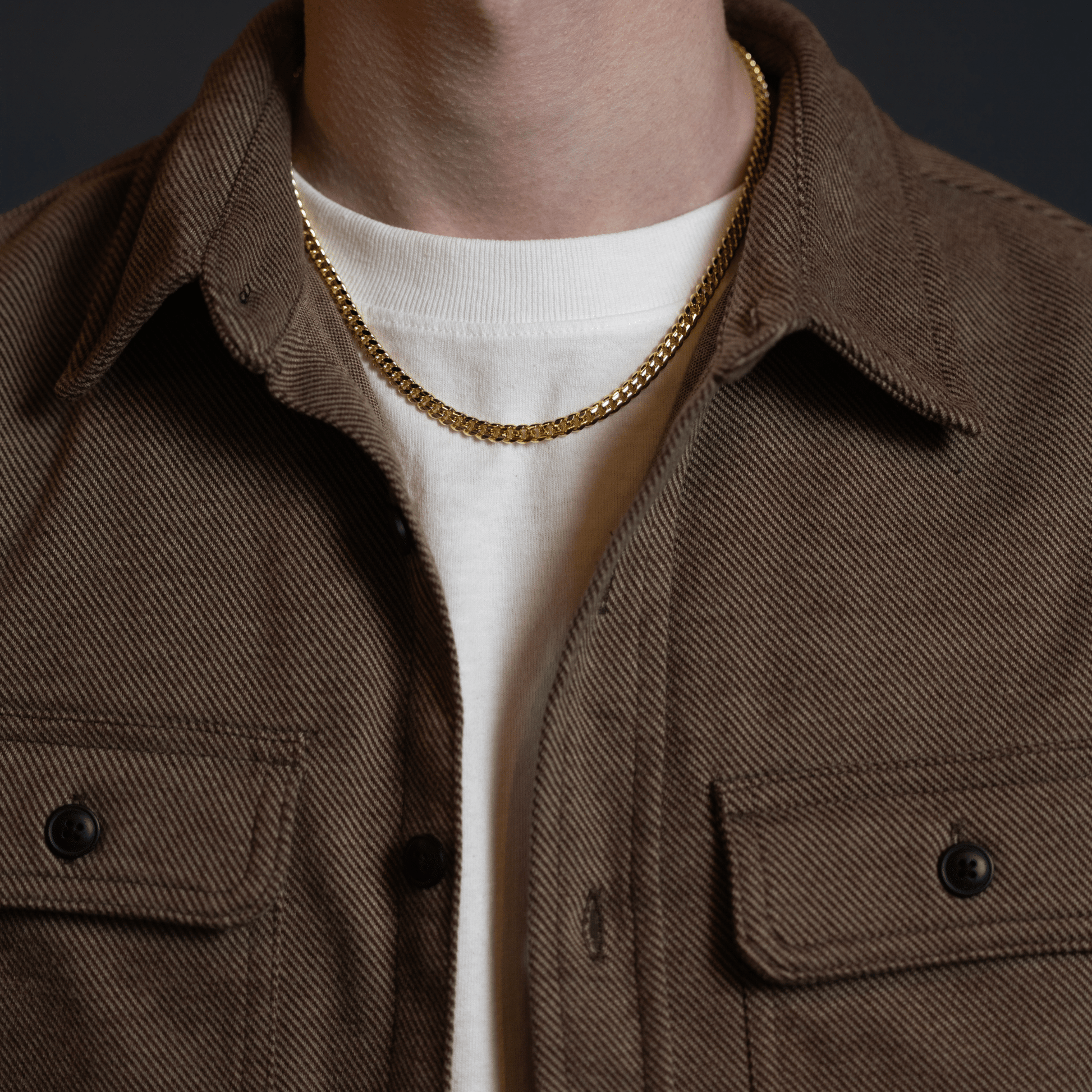 Gold Cuban link chain necklace worn with a casual jacket, featuring a sleek polished finish and classic men’s jewelry style.