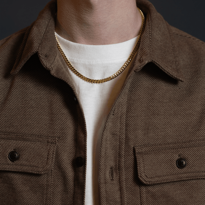 Gold Cuban link chain necklace worn with a casual jacket, featuring a sleek polished finish and classic men’s jewelry style.