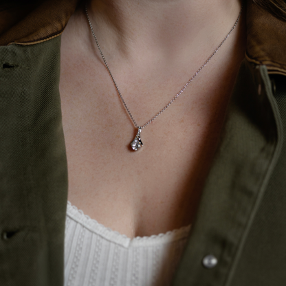 silver chain necklace with a pendant featuring a clear gemstone, model in an olive green shirt over a white top.