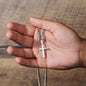Hand holding a silver cross necklace against a wooden background