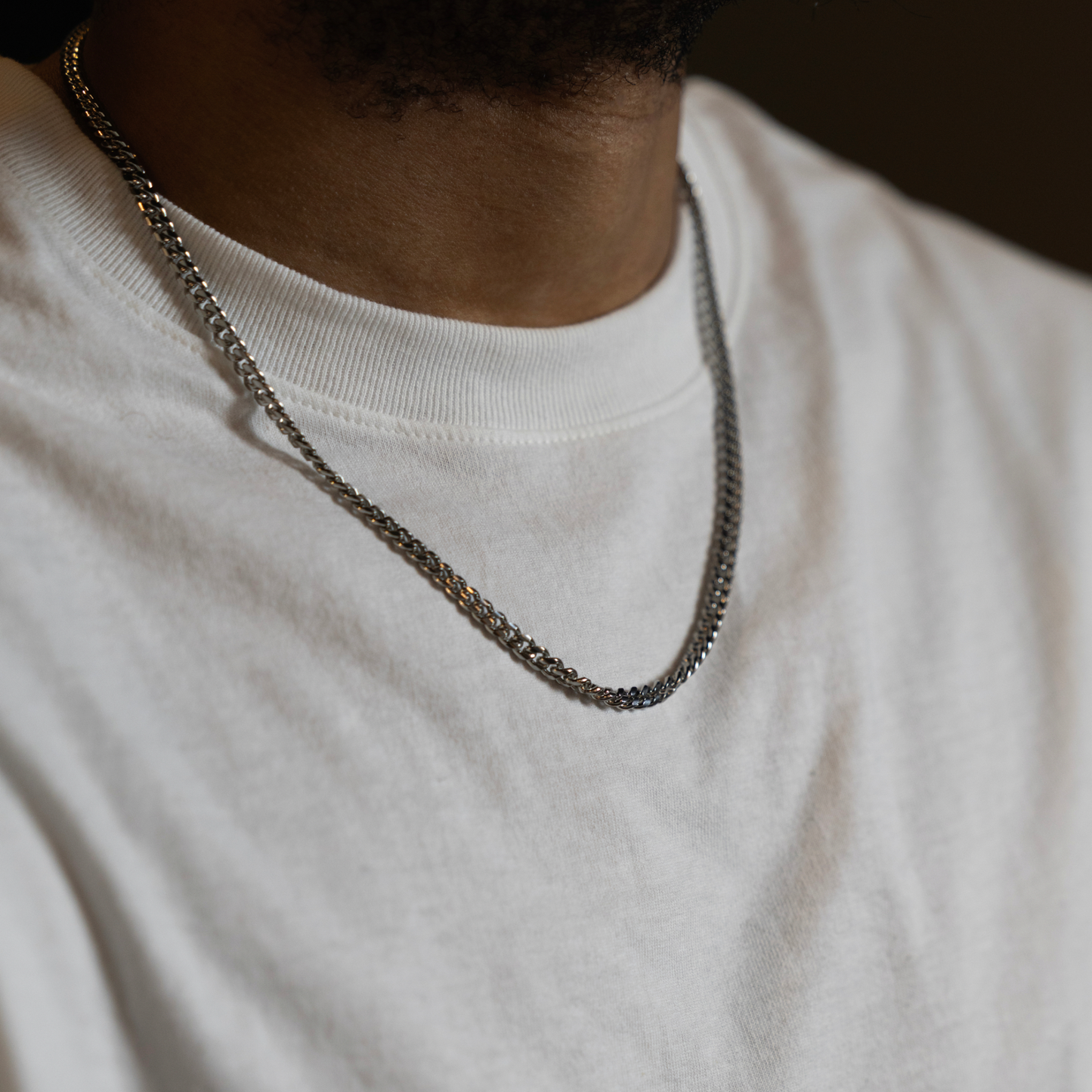 A close-up shot of a person wearing a silver-toned chain necklace over a white crewneck t-shirt.