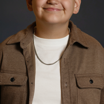 A close-up of a person wearing a brown corduroy overshirt over a white t-shirt, accessorized with a silver chain necklace, against a dark gray background.