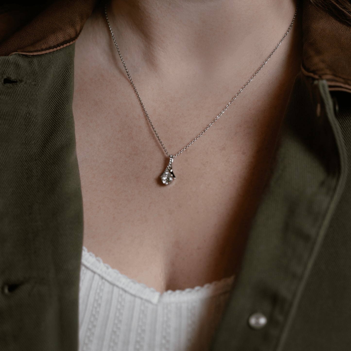 silver chain necklace with a pendant featuring a clear gemstone, model in an olive green shirt over a white top.