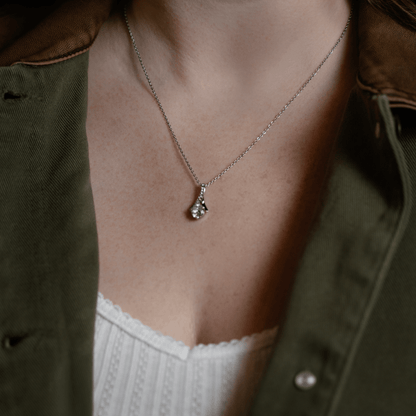 silver chain necklace with a pendant featuring a clear gemstone, model in an olive green shirt over a white top.