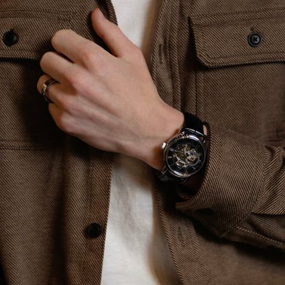 Men's black skeleton watch with genuine leather strap worn with a brown jacket