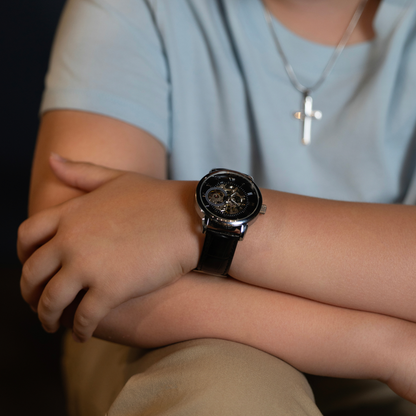 Black skeleton mechanical watch with leather strap on a young man's wrist.