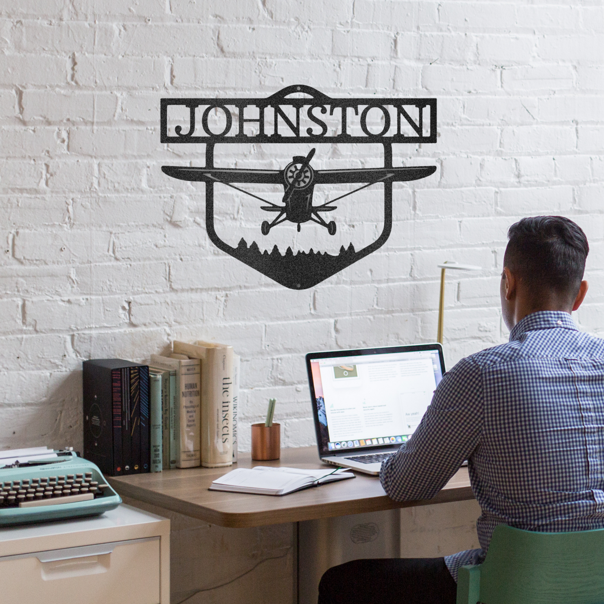 Decorative metal sign with airplane silhouette and 'Johnston' text on a white brick wall background With man sitting