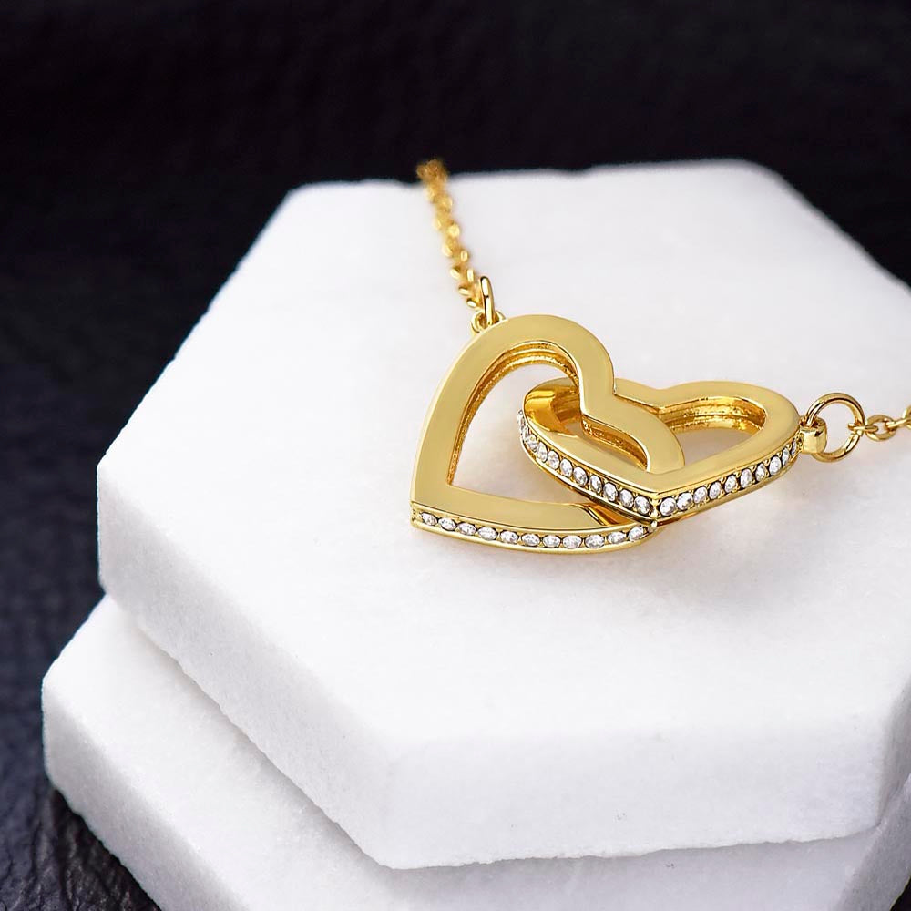 Close-up of gold interlocking hearts necklace with crystal accents displayed on white gift box
